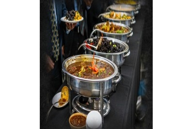 Buffet avec plusieurs plats chauds en marmites en inox, accompagné de sauces et d'assiettes en arrière-plan.