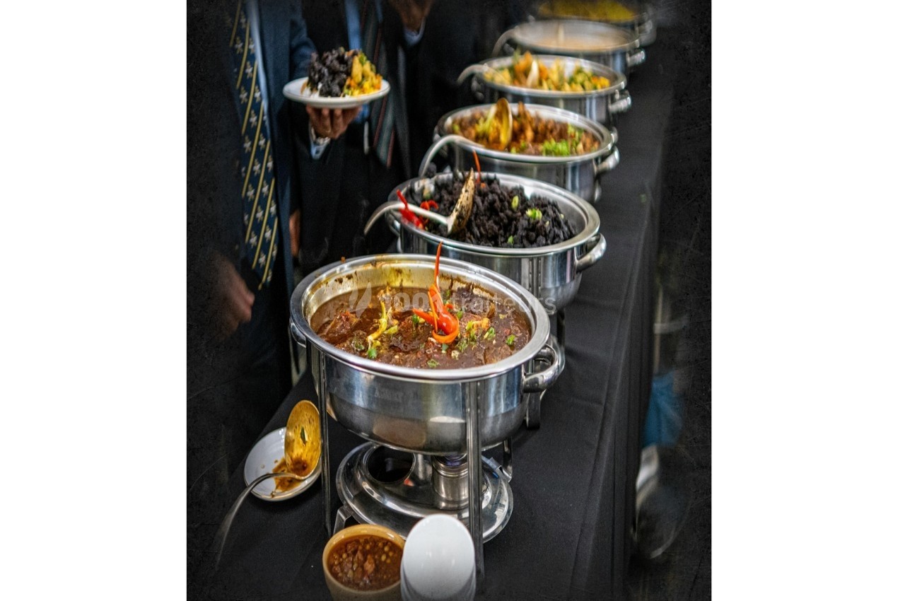 Buffet avec plusieurs plats chauds en marmites en inox, accompagné de sauces et d'assiettes en arrière-plan.
