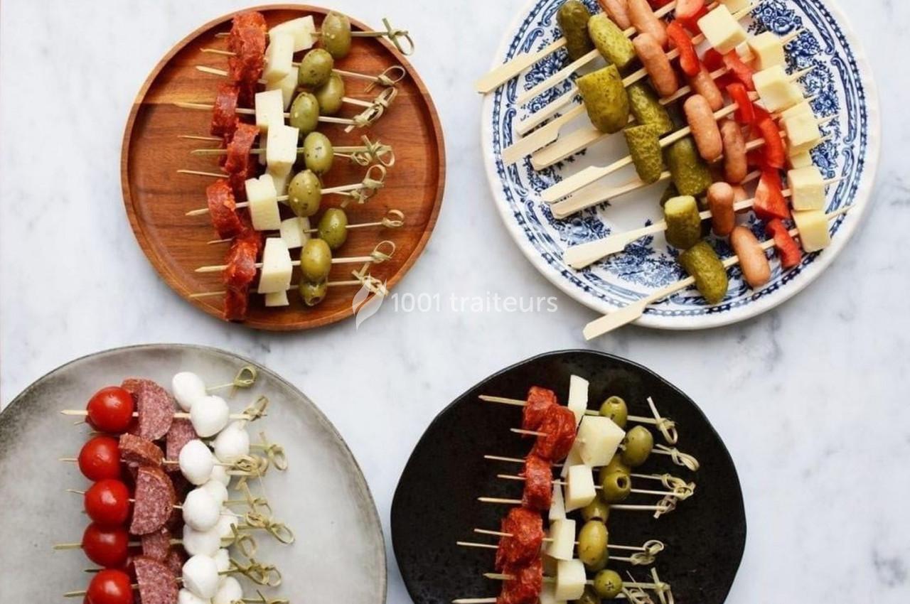 Assortiment de brochettes apéritives avec légumes, fromages, charcuteries et olives sur des assiettes variées.