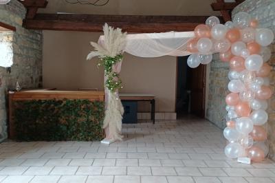 Salle de réception en pierre avec tables dressées, décorations florales et bougies, éclairée par la lumière naturelle.