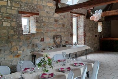 Salle de réception en pierre avec tables dressées, décorations florales et bougies, éclairée par la lumière naturelle.
