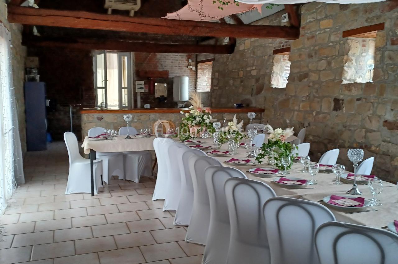Salle de réception en pierre avec tables décorées de nappes blanches, fleurs et vaisselle pour un événement festif.
