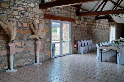 Salle de réception en pierre avec tables dressées, décorations florales et bougies, éclairée par la lumière naturelle.