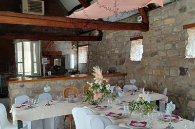 Salle de réception en pierre avec tables dressées, décorations florales et bougies, éclairée par la lumière naturelle.