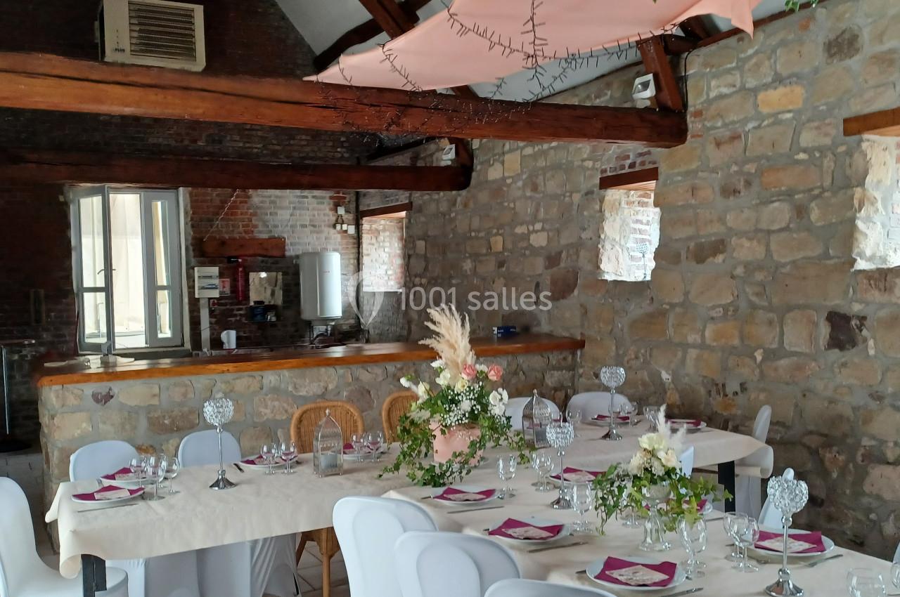Salle en pierre avec une grande table dressée pour un repas, décorée de fleurs et de serviettes roses.
