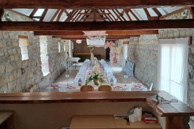 Salle de réception en pierre avec tables dressées, décorations florales et bougies, éclairée par la lumière naturelle.