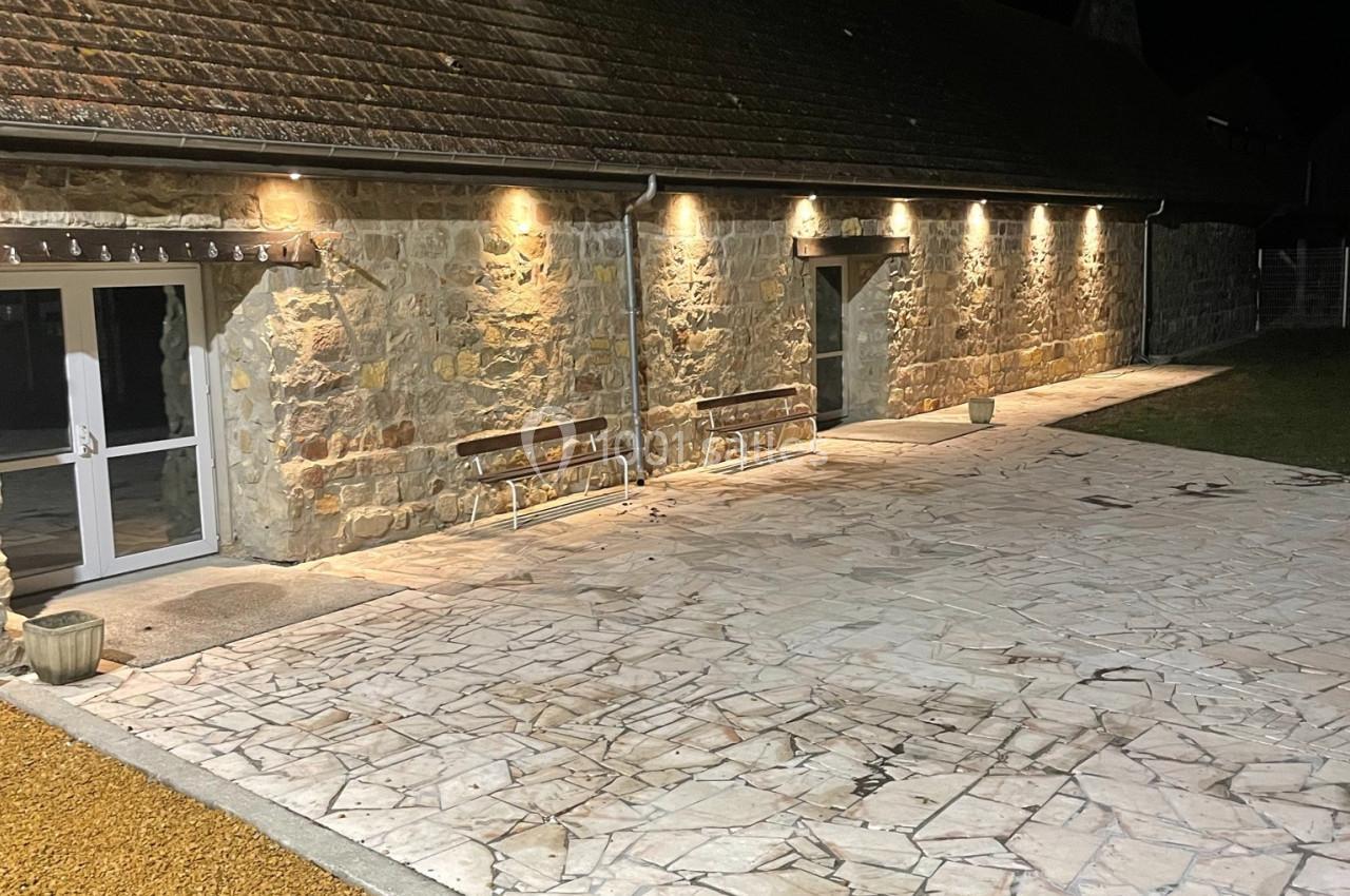 Cour en pierre éclairée la nuit, bordée par un bâtiment en pierre avec des lumières murales.