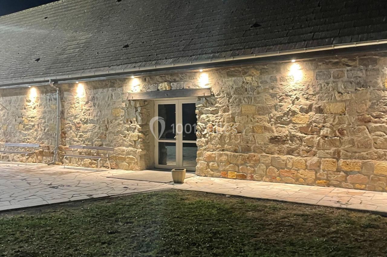 Façade en pierre d'un bâtiment éclairé par des appliques murales, avec une porte vitrée au centre, de nuit.