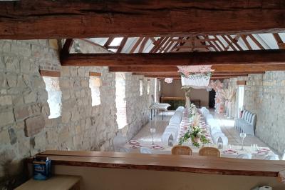 Salle de réception en pierre avec tables dressées, décorations florales et bougies, éclairée par la lumière naturelle.