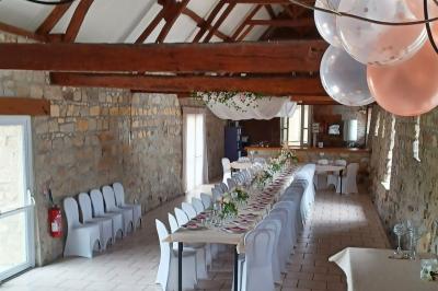Salle de réception en pierre avec tables dressées, décorations florales et bougies, éclairée par la lumière naturelle.