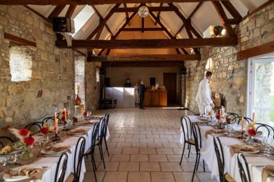 Salle de réception en pierre avec tables dressées, décorations florales et bougies, éclairée par la lumière naturelle.