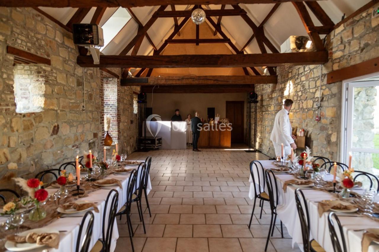 Salle en pierre avec tables dressées pour un repas, décorée de fleurs et bougies, avec un bar en arrière-plan.