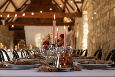 Salle de réception en pierre avec tables dressées, décorations florales et bougies, éclairée par la lumière naturelle.