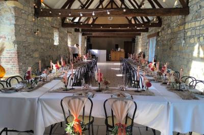Salle de réception en pierre avec tables dressées, décorations florales et bougies, éclairée par la lumière naturelle.