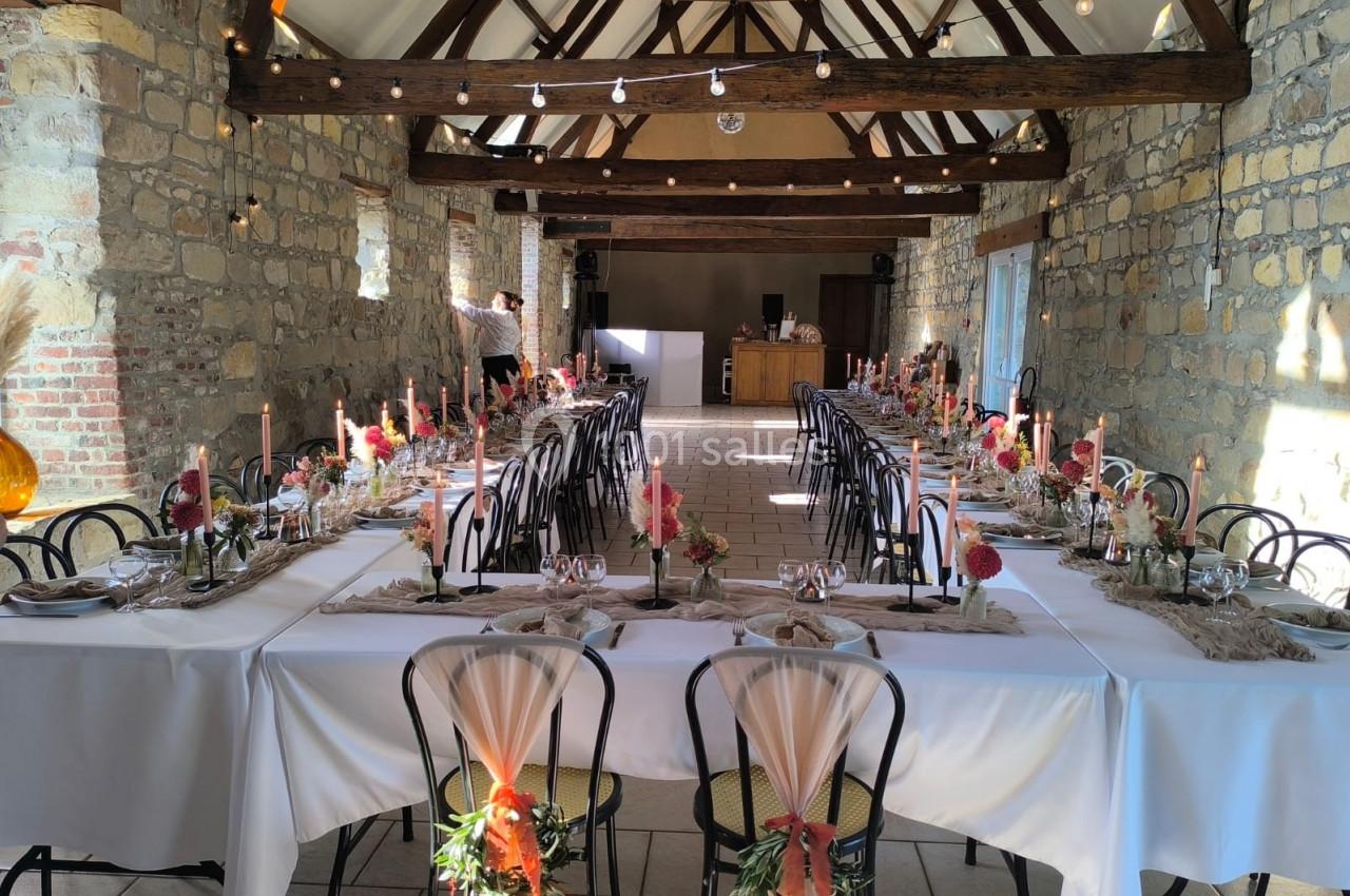 Salle de réception en pierre avec tables dressées, décorations florales et bougies, éclairée par la lumière naturelle.