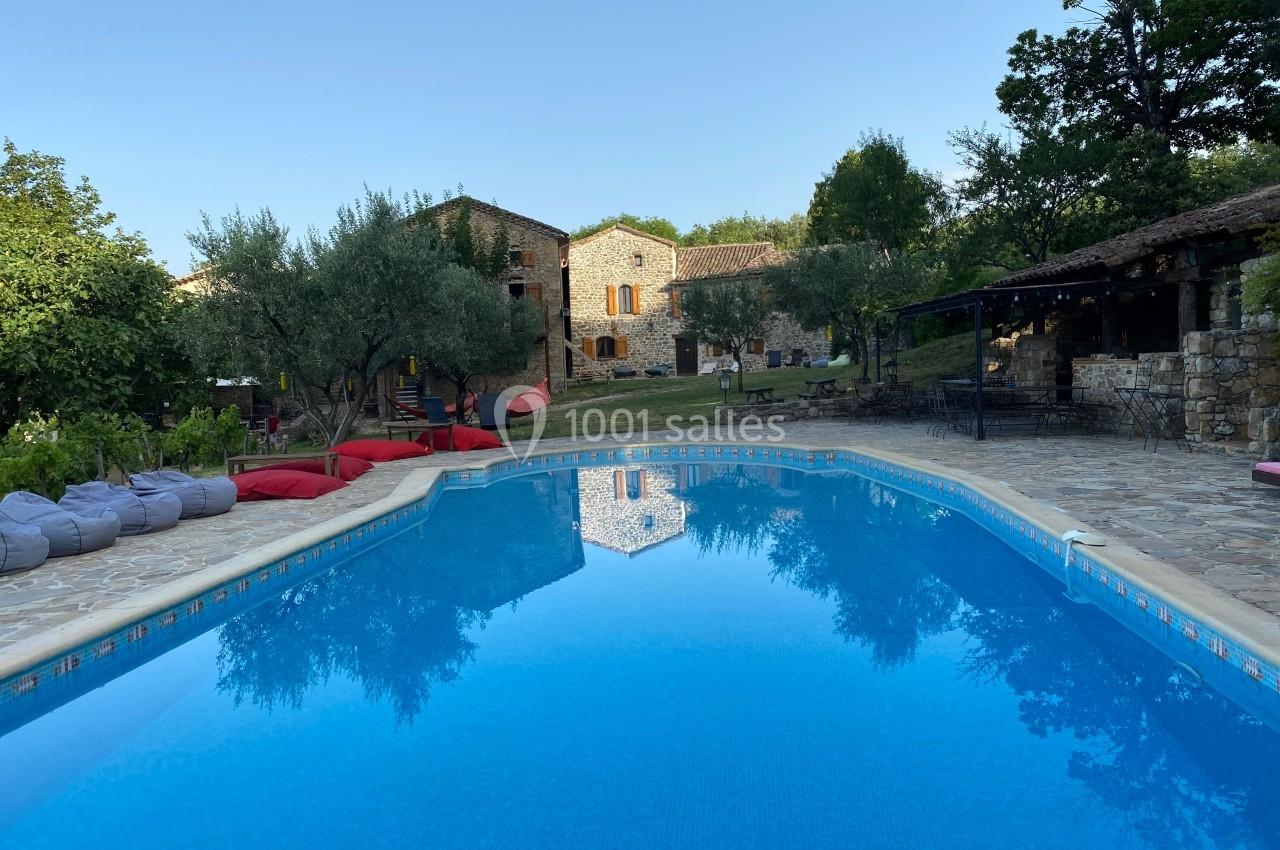 Piscine extérieure entourée de pierres et de verdure, avec des bâtiments en pierre en arrière-plan.