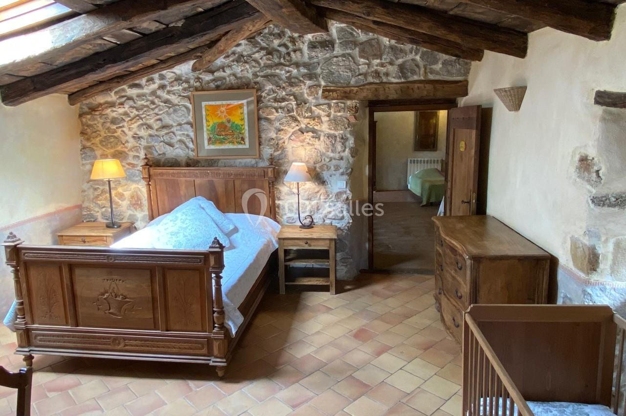 Chambre rustique avec lit en bois sculpté, murs en pierre, poutres apparentes et mobilier en bois.