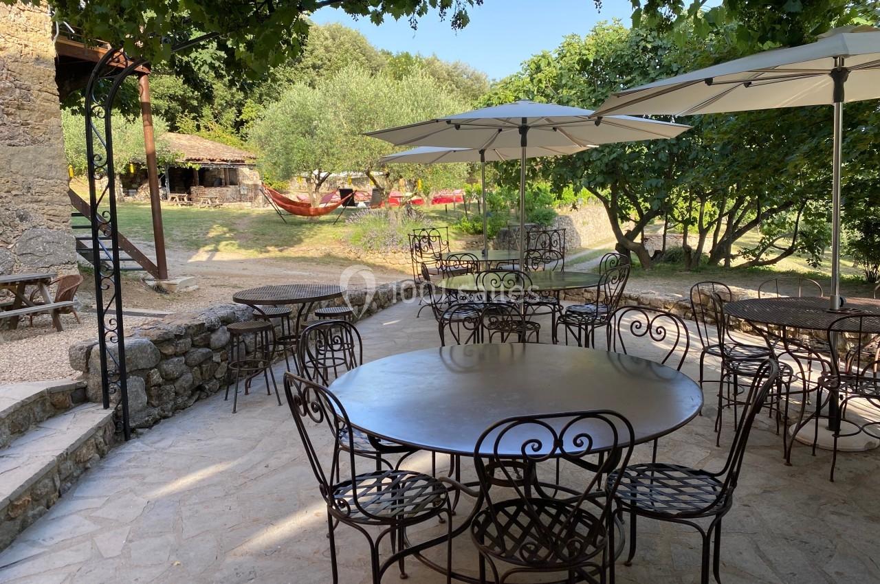 Terrasse en plein air avec tables et chaises en fer forgé, entourée de verdure et équipée de parasols.