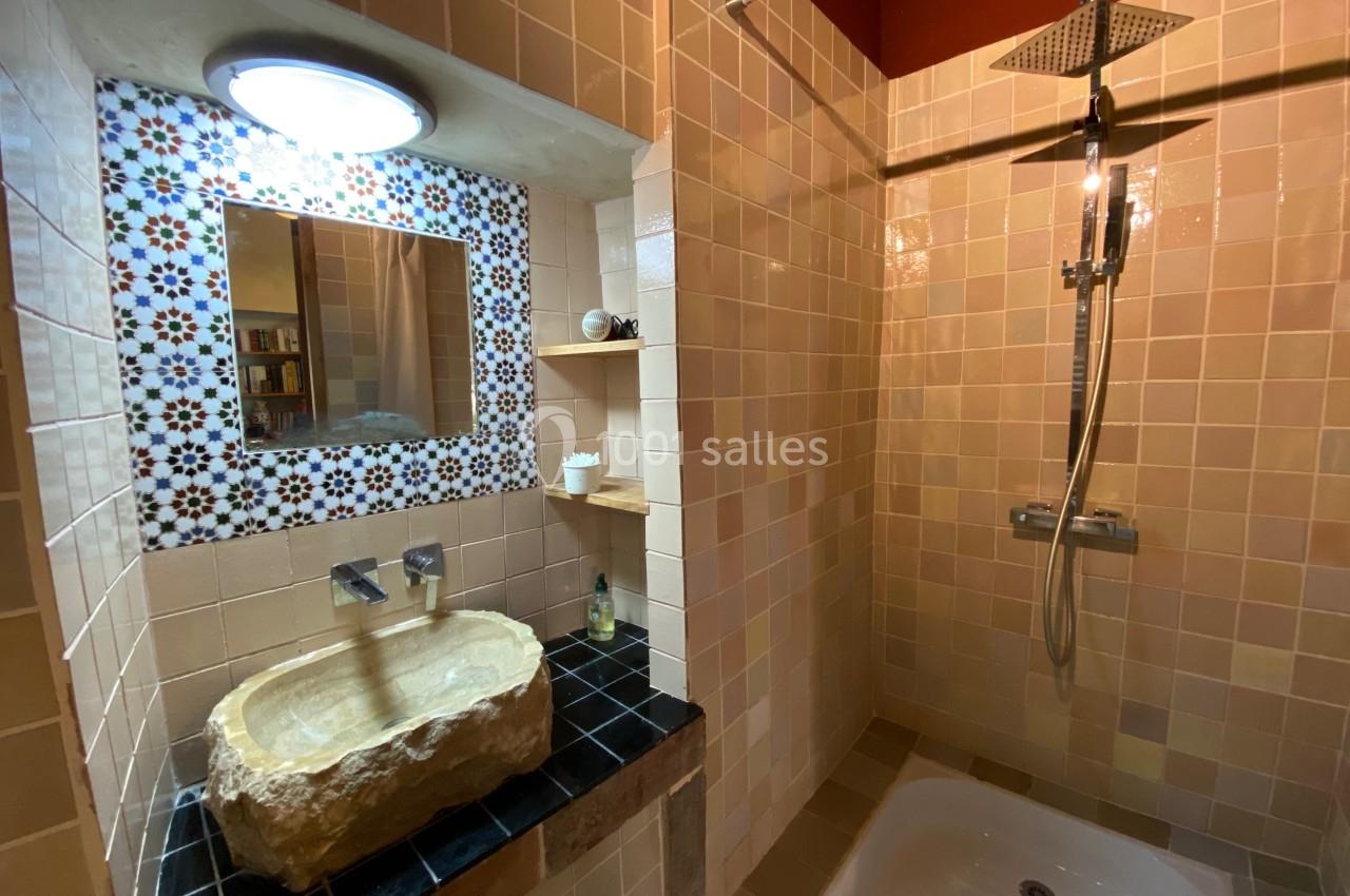Salle de bain avec lavabo en pierre, miroir encadré de mosaïques, étagères en bois et douche à l'italienne.