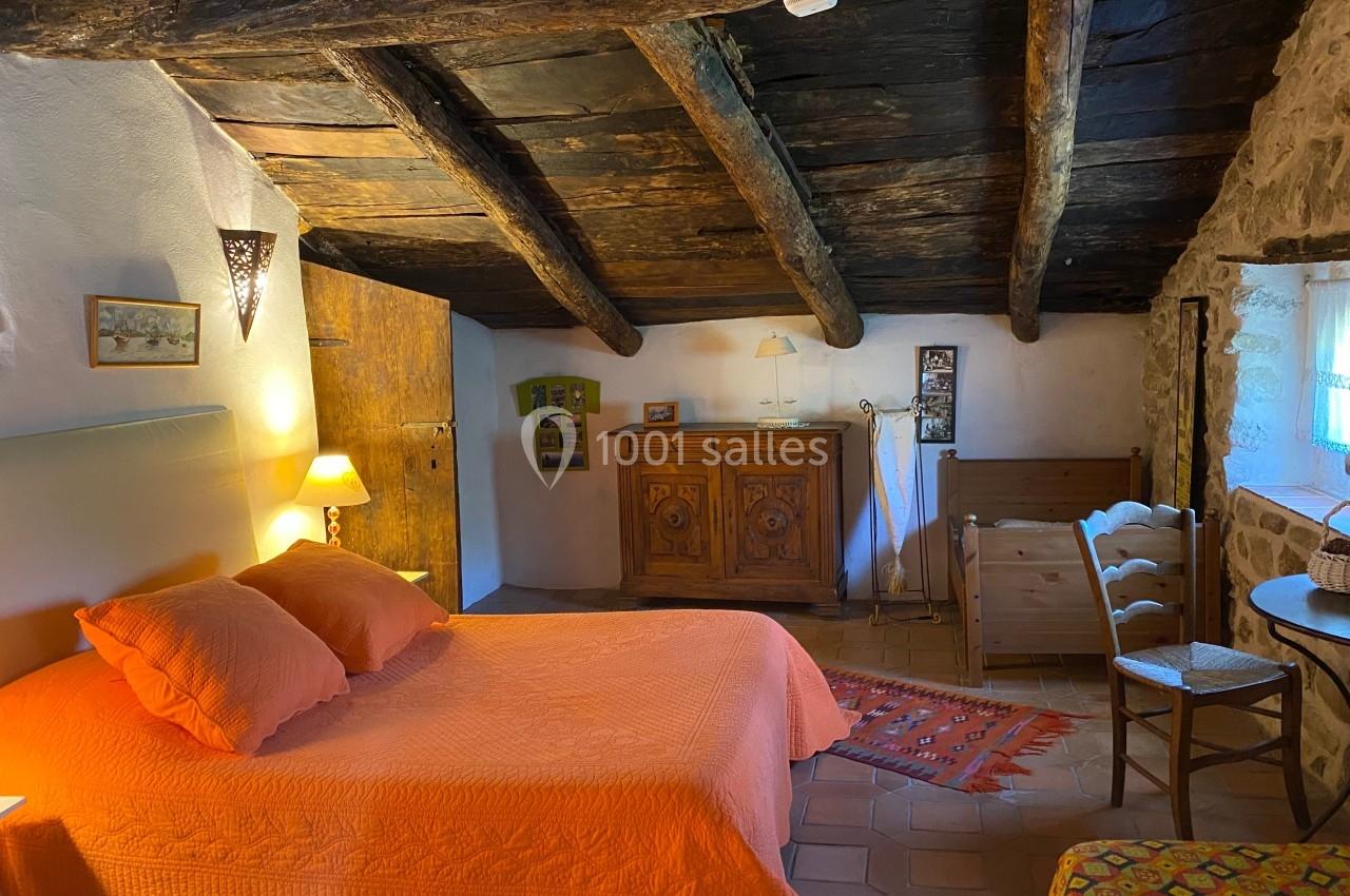Chambre rustique avec poutres apparentes, lit double orange, mobilier en bois et lumière douce.