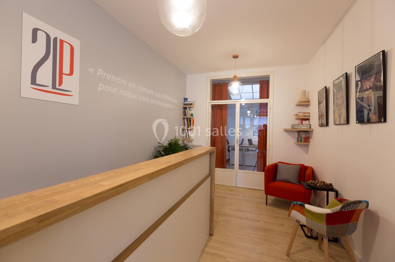 Vue d'un espace d'accueil lumineux avec comptoir en bois, fauteuil rouge et décorations murales.