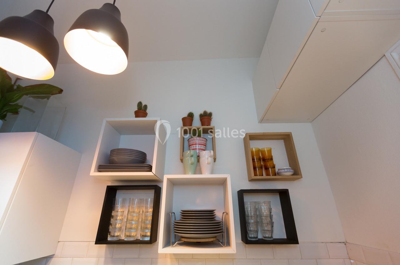 Étagères murales avec vaisselle, verres et plantes en pot dans une cuisine moderne éclairée par des suspensions.