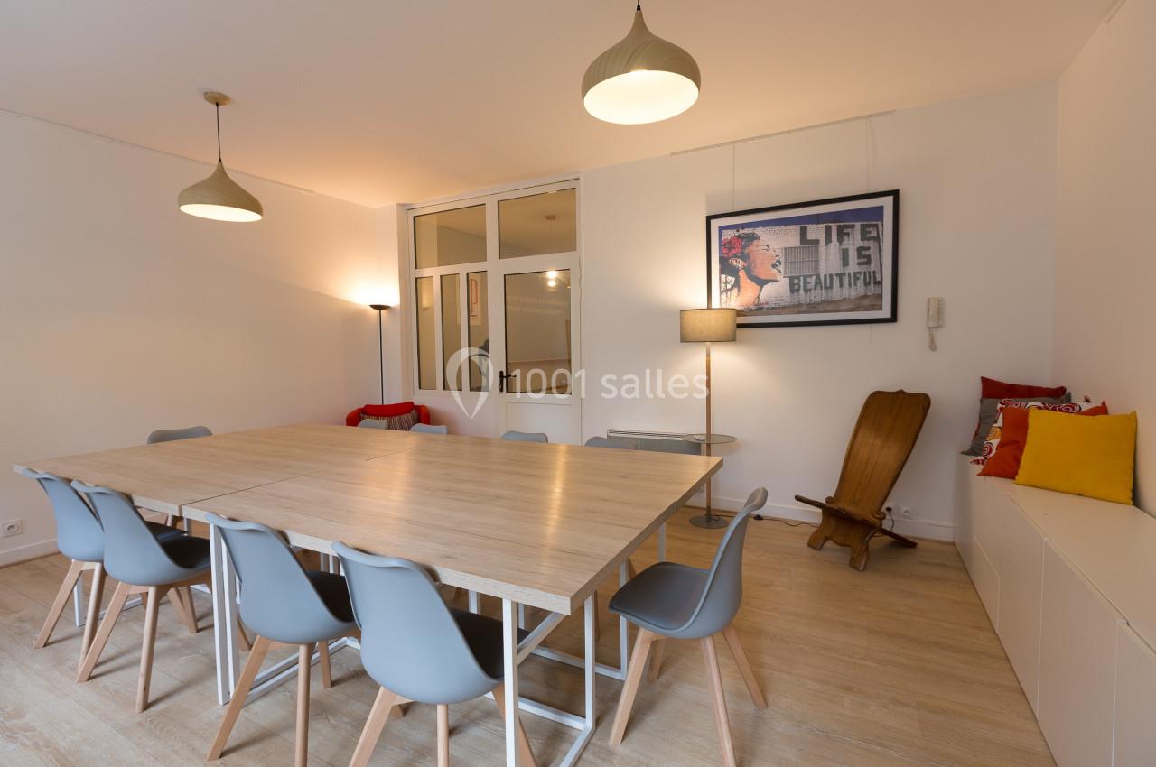 Salle de réunion lumineuse avec une grande table en bois entourée de chaises grises et des éléments décoratifs modernes.