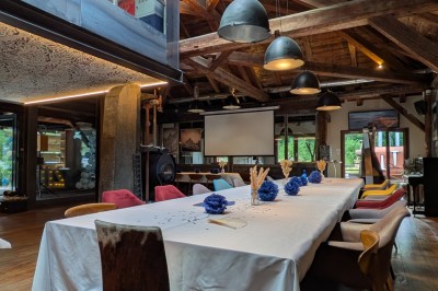 Table en bois avec verres à pied, carafe de boisson, herbes fraîches et décor intérieur lumineux et végétalisé.