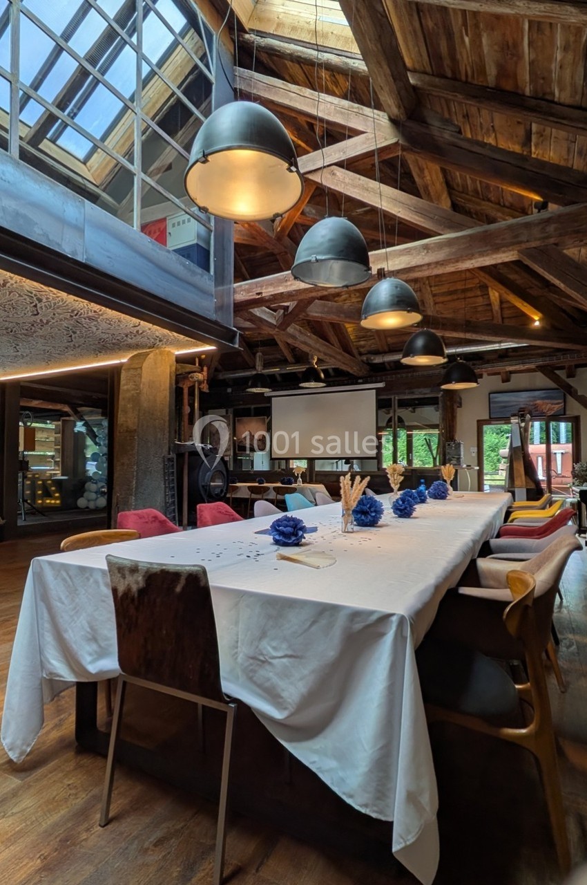 Salle de réunion chaleureuse avec une grande table dressée, des chaises variées et un plafond en bois apparent.