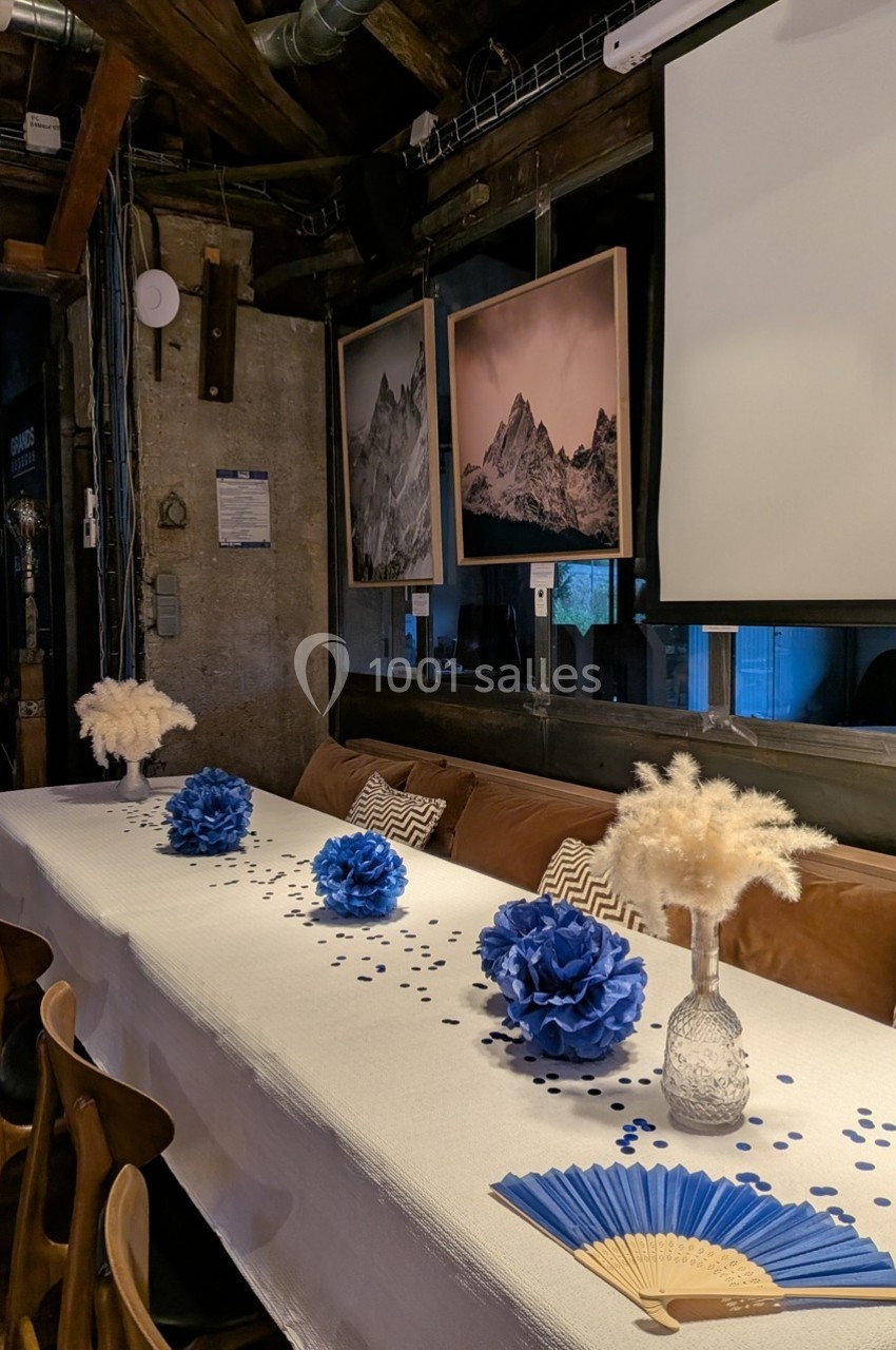 Table décorée avec des fleurs bleues, pampas et confettis, dans une salle au style rustique avec des cadres muraux.