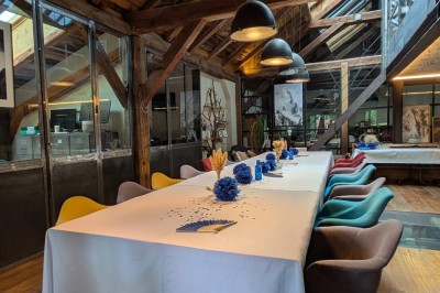 Table en bois avec verres à pied, carafe de boisson, herbes fraîches et décor intérieur lumineux et végétalisé.