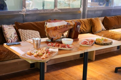 Table en bois avec verres à pied, carafe de boisson, herbes fraîches et décor intérieur lumineux et végétalisé.