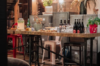Table en bois avec verres à pied, carafe de boisson, herbes fraîches et décor intérieur lumineux et végétalisé.