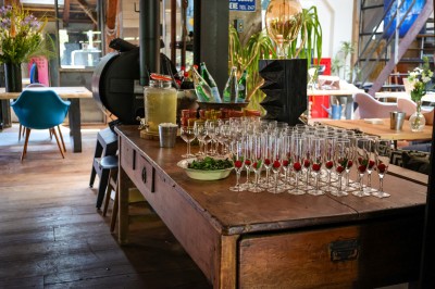 Table en bois avec verres à pied, carafe de boisson, herbes fraîches et décor intérieur lumineux et végétalisé.