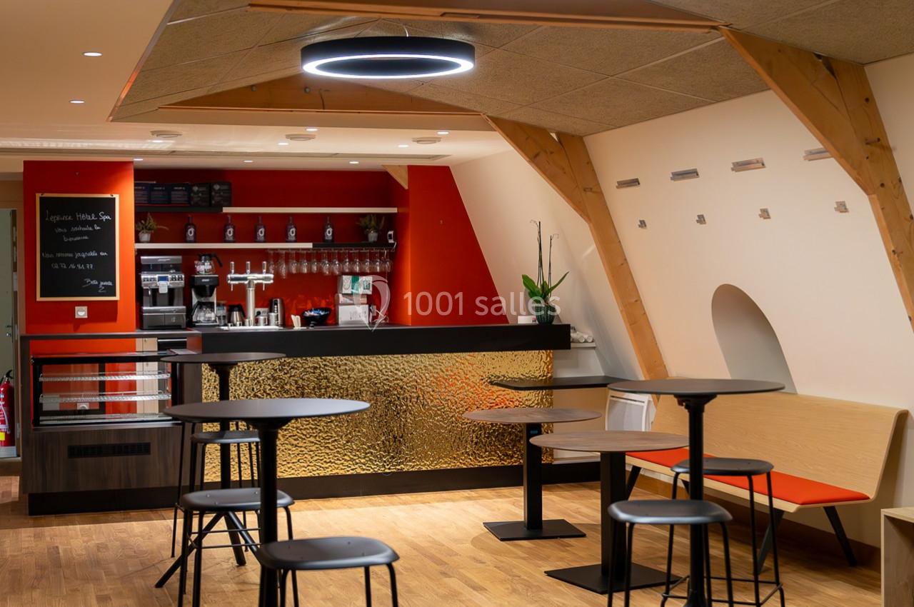 Espace café moderne avec comptoir rouge et noir, tables hautes, chaises et éclairage circulaire suspendu.