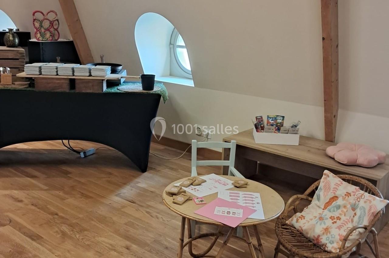 Coin aménagé avec une petite table, des chaises en rotin, des documents et des décorations dans une pièce lumineuse.