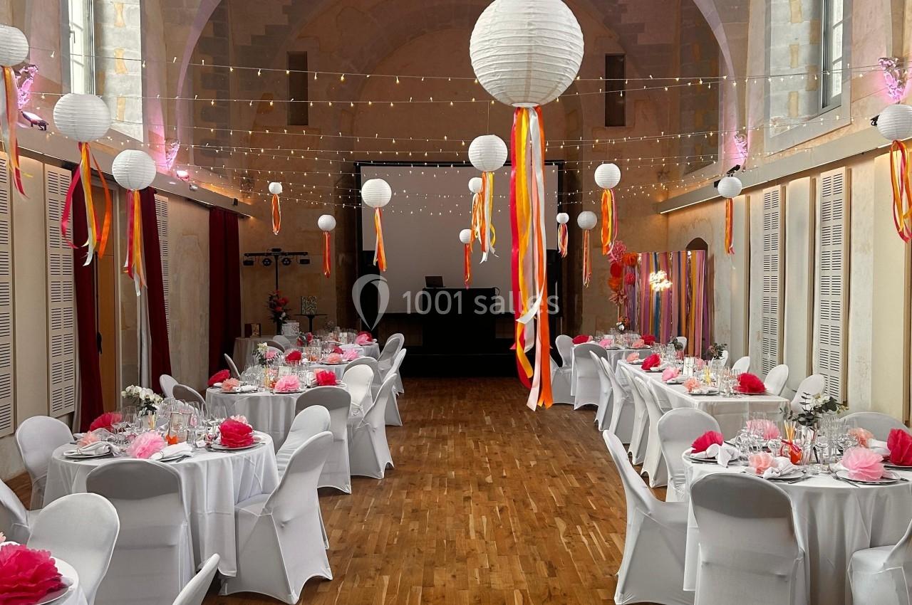 Salle de réception décorée avec des tables dressées, des lanternes suspendues et des rubans colorés.