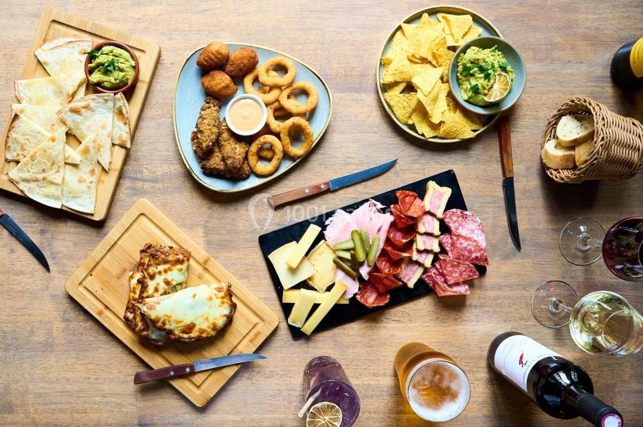 Assortiment de plats variés sur une table en bois, incluant charcuterie, fromages, nachos, quesadillas et boissons.