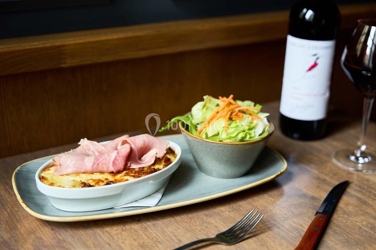 Plat de gratin garni de jambon accompagné d'une salade verte et d'un verre de vin rouge sur une table en bois.