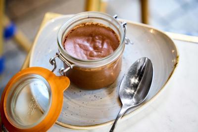 Pot de mousse au chocolat dans un bocal en verre ouvert, posé sur une assiette avec une cuillère en métal.