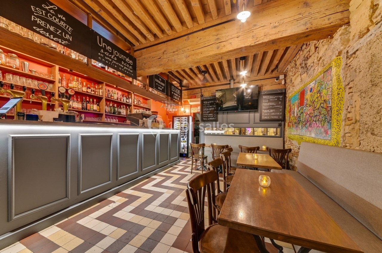 Intérieur d'un café avec comptoir, tables en bois, murs en pierre et éclairage chaleureux.
