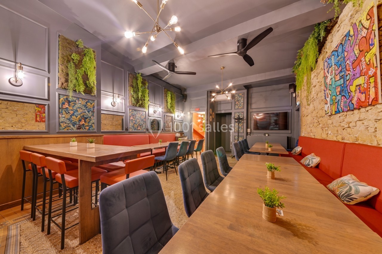 Salle de restaurant moderne avec tables en bois, chaises colorées, murs décorés et plantes suspendues.