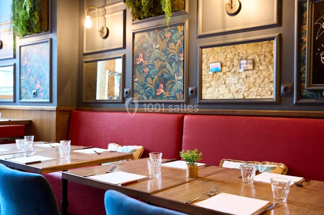 Banquettes rouges et tables en bois dans un restaurant décoré de miroirs, motifs floraux et plantes suspendues.