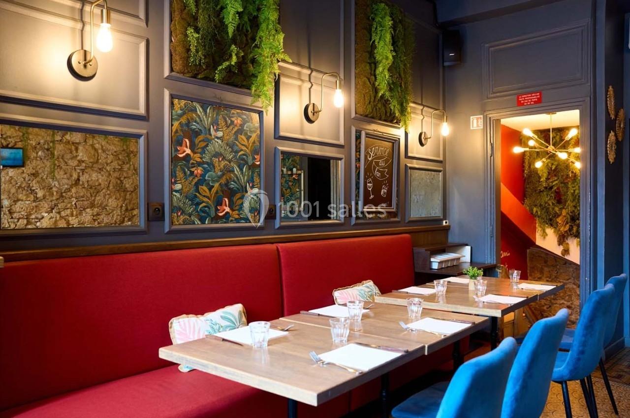 Salle de restaurant avec banquettes rouges, chaises bleues, murs décorés de plantes et papiers peints colorés.