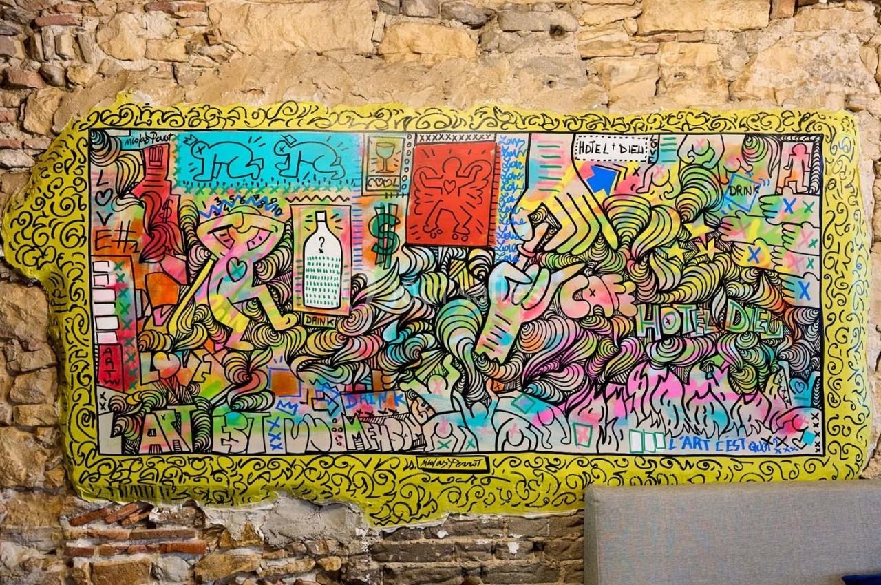 Fresque colorée et abstraite peinte sur un mur en pierre, mêlant motifs, textes et formes variées.