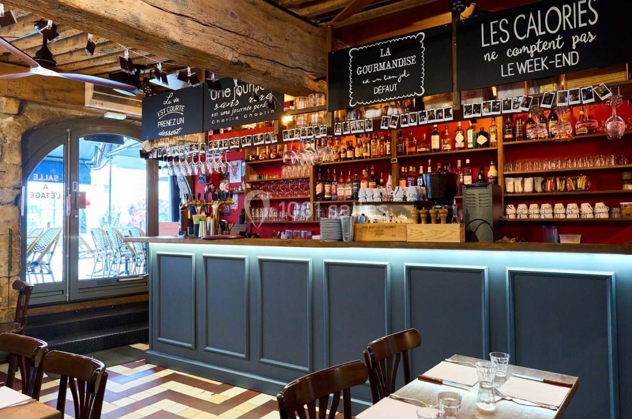 Intérieur d'un café-restaurant avec un comptoir en bois, étagères remplies de bouteilles et ardoises décoratives au mur.