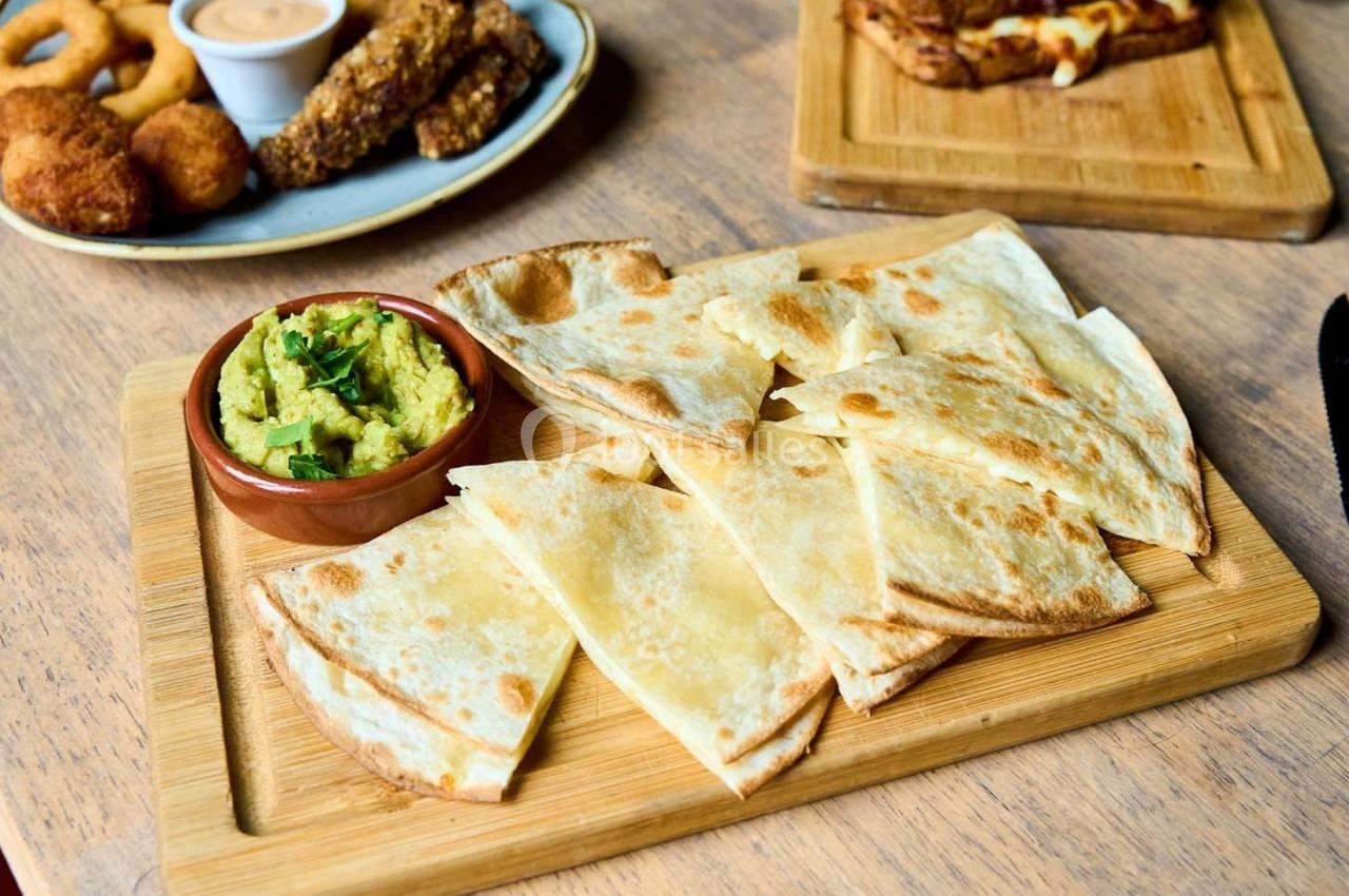 Assiette de quesadillas dorées servies avec un bol de guacamole sur une planche en bois.