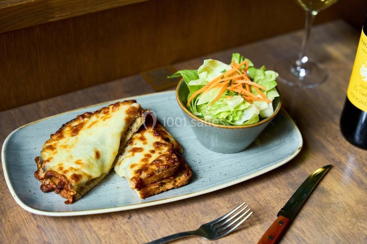 Croque-monsieur gratiné au fromage accompagné d'une salade verte avec carottes râpées, servi sur une table en bois.