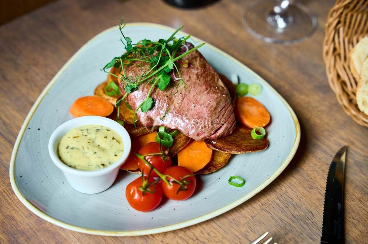 Assiette de viande grillée avec légumes rôtis, tomates cerises, sauce en ramequin et garniture de pousses vertes.