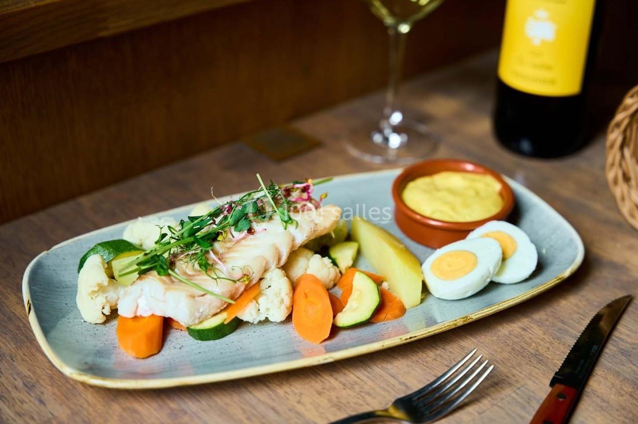 Assiette de poisson accompagné de légumes cuits, œufs durs, sauce jaune et verre de vin en arrière-plan.